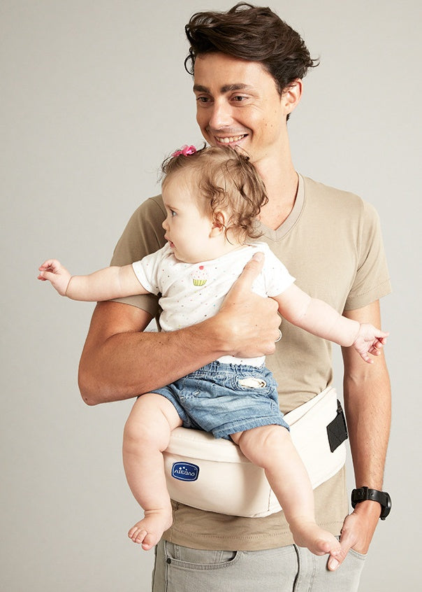 Father holding baby in ergonomic baby waist stool carrier with anti-skid design and mesh pocket for small objects.